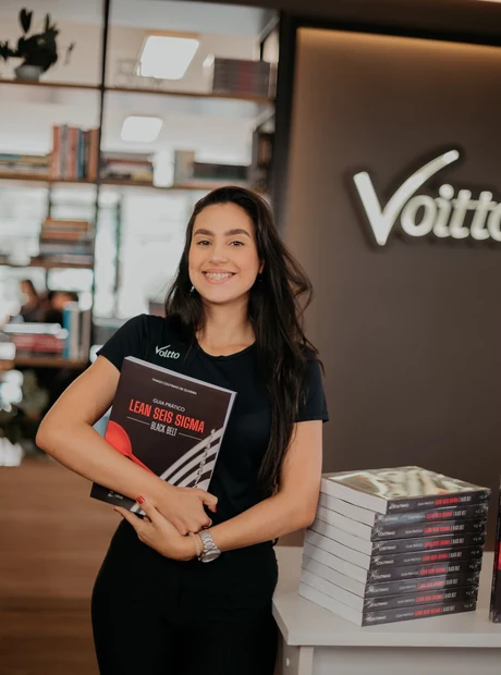 Profissional da Voitto com o Guia Prático Lean Seis Sigma Black Belt em mãos, ao lado de uma pilha de exemplares do livro.