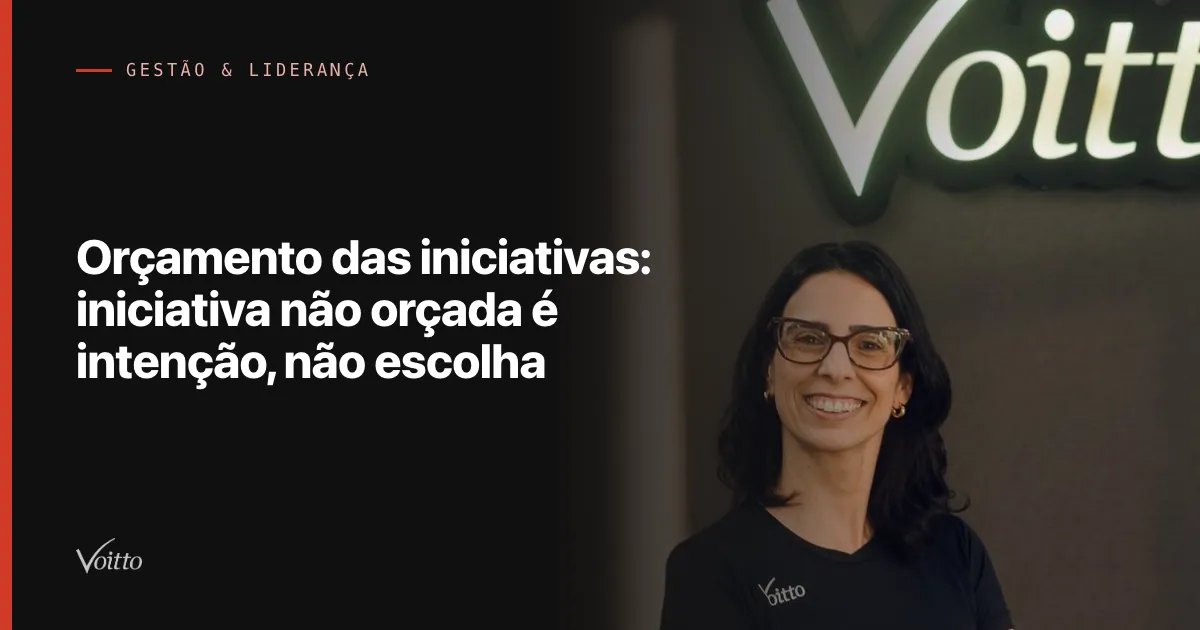 Colaboradora da Voitto de óculos e camiseta preta, sorrindo diante do letreiro Voitto com a estante ao fundo, com o texto Orçamento das iniciativas: iniciativa não orçada é intenção, não escolha sobre fundo escuro à esquerda