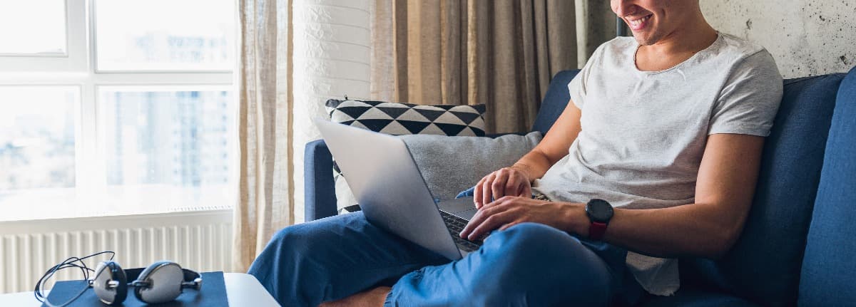 Homem trabalhando em homeoffice sentado em um sofa azul. 