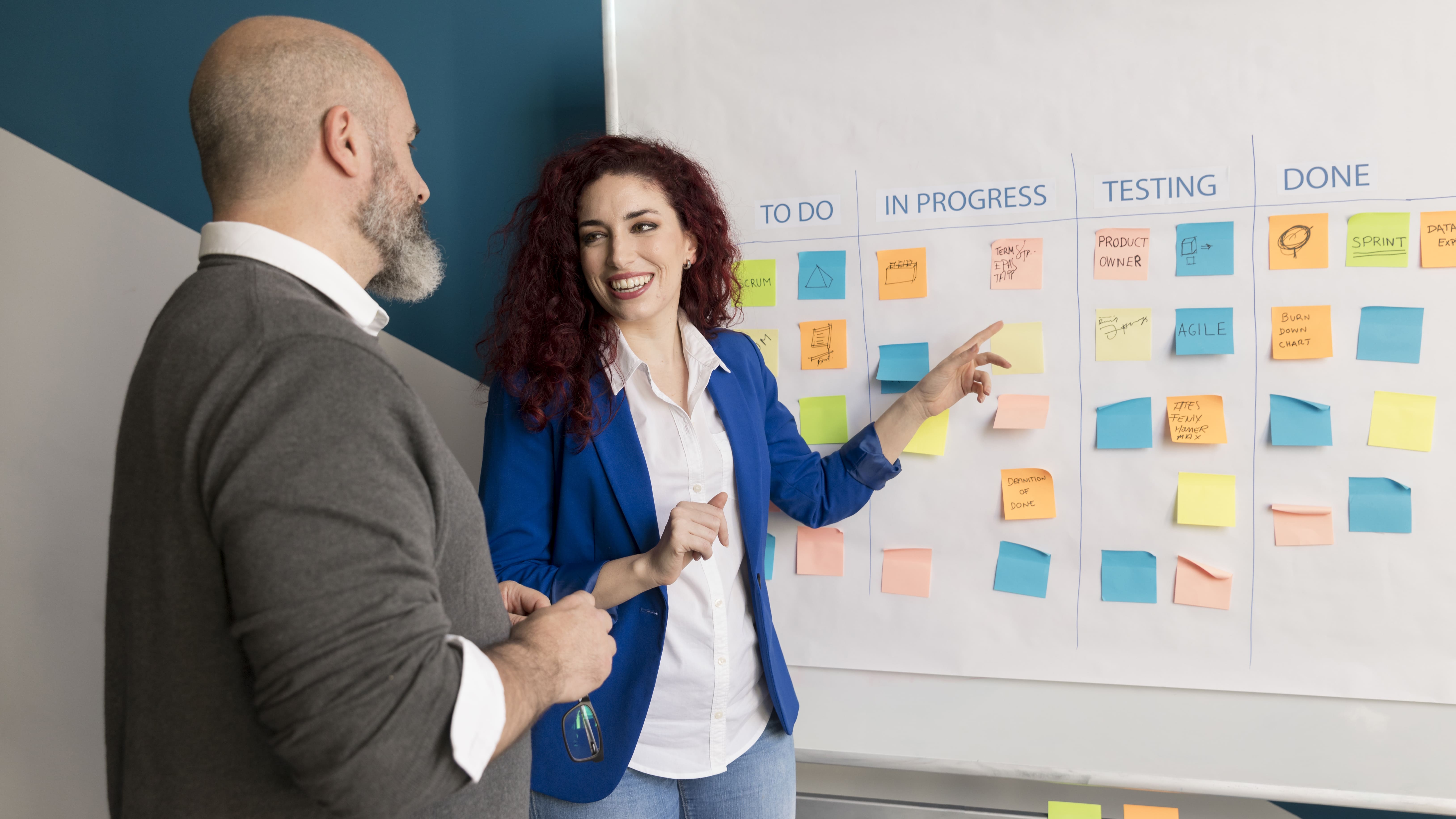 Mulher apontando para um quadro Kanban com vários post-its coloridos Mulher apontando para um quadro Kanban com vários post-its coloridos